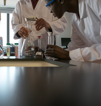 Young male and female scientists preparing experiment with sample bottles in laboratory, cropped