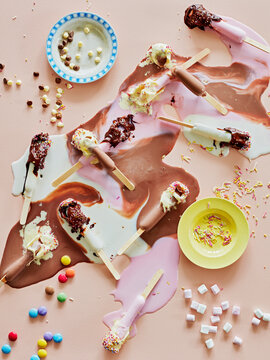 Chocolate top ice lollies melting and sprinkles on table