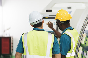 Caucasian and African production workers discuss together at CNC machine in factory. Concept of industry work, diversity group of people with copy space