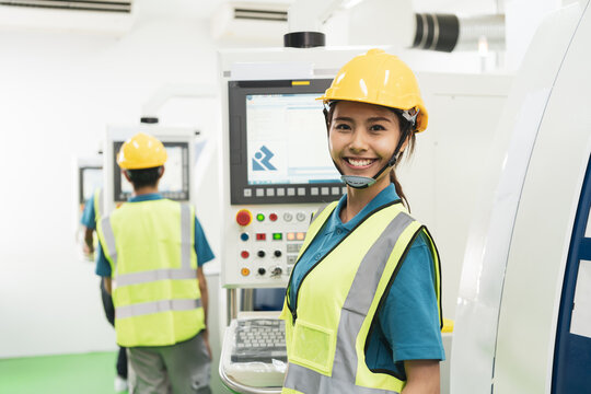 Asian female worker in uniform with vest and hardhat smile at CNC machine in factory production line. Concept of industry factory with copy space