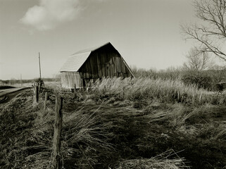 Sweeping Barn. A sepia toned black and white landscape of a barn surrounded by windswept tall grass making interesting shapes. Near Youngstown, Missouri USA, 1979.