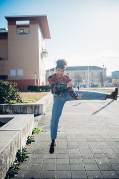 Young woman jumping and kicking leg on urban sidewalk, full length portrait