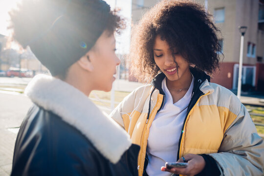 Two cool young female friends looking at smartphone in urban street