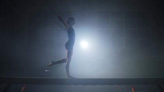 teen girl gymnast is performing jump on balance beam, training in sport school and preparing to olympic games