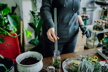 Woman filling glass bottle with plants in nursery