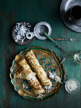 Rustic low key still life with plate of grated coconut pancakes on table, overhead view