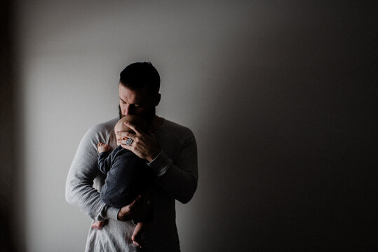 Young man carrying baby son in arms, low key