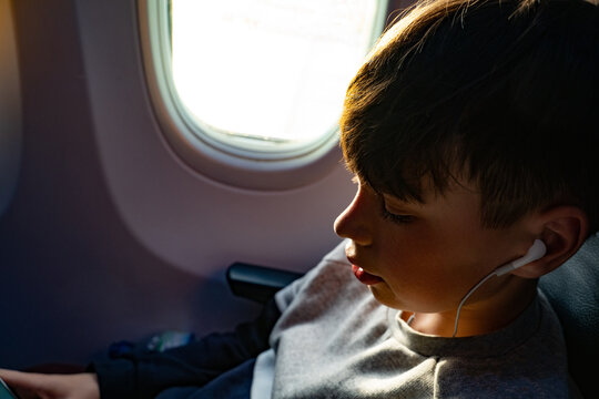 Teenage boy listening to music on earphones during airplane journey, close up
