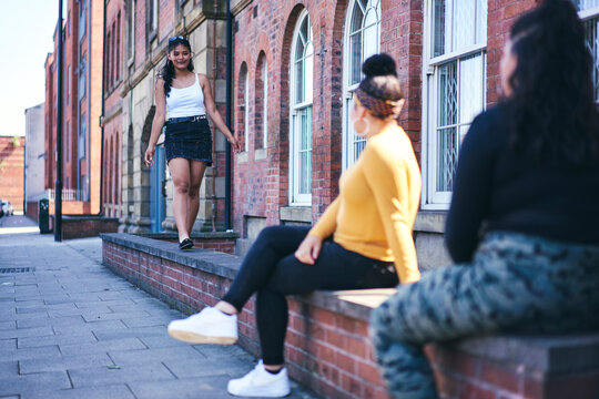 Young woman walking along wall watched by teenage sisters
