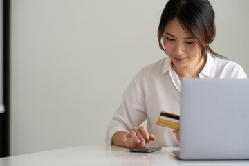 Happy woman using smart phone and laptop computer and credit card for shopping online at home
