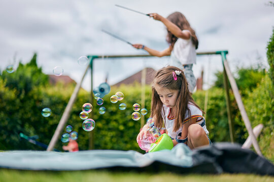 Girl playing with soap bubbles, sister in background with diabolo