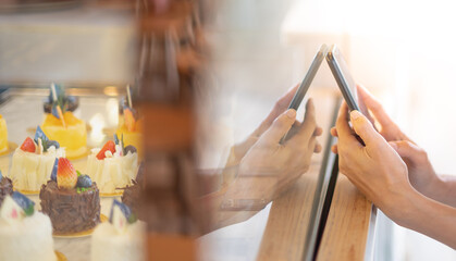 Female hand use the mobile phone for take photo with the homemade cake through the clear shelf for share on the social media.