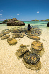 Okinawa girl sitting on the rocks at Hoshizuna beach with its crystal clear waters, Iriomote island.
