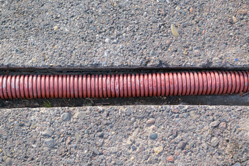 Corrugated pipe in the channel. Horizontal recess. Surface material - asphalt with pebbles. The concept of laying a cable, connecting devices, internet, communication, electricity. - obrazy, fototapety, plakaty