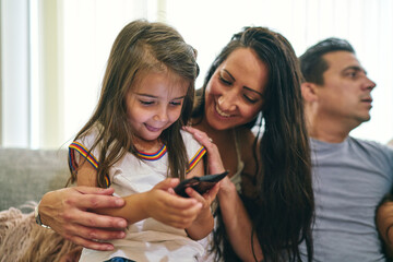 Mother watching daughter play computer game, father in background