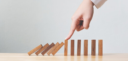 Hand stopping wooden domino business crisis effect or risk protection concept - obrazy, fototapety, plakaty