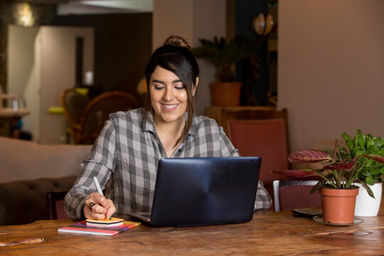 Woman writing notes and working on laptop in co-working space