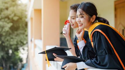 The Asian university graduates in graduation gown and a mortarboard cap with a degree certificate...