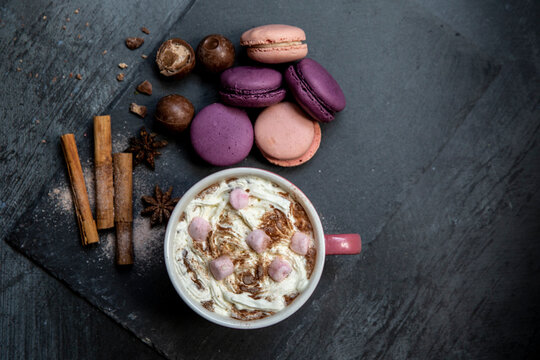 Hot chocolate topped with marshmallows and cream, macaroons, cinnamon sticks, star anise