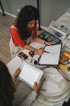 Two mid adult women looking at plans and digital tablet in their new shop, high angle view