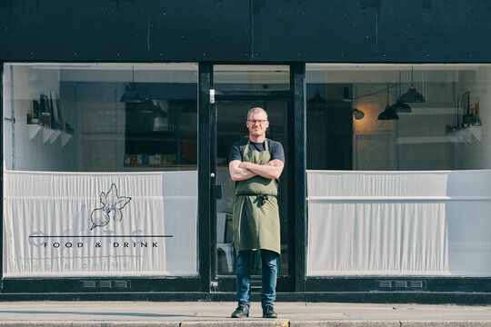 Restaurant owner with arms crossed at shopfront