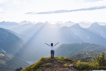 Female hiker raising arms against sun on peak, Winchester Mountain, North Cascades, Washington, USA