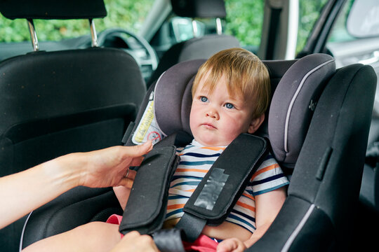 Toddler being strapped into a child car seat in the back of a family car. 