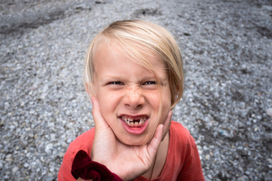 Boy with a missing front tooth, making faces at person squeezing his face