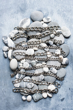 Grey and white pebbles in an oval shape with silver metal chains lying across them in bands.