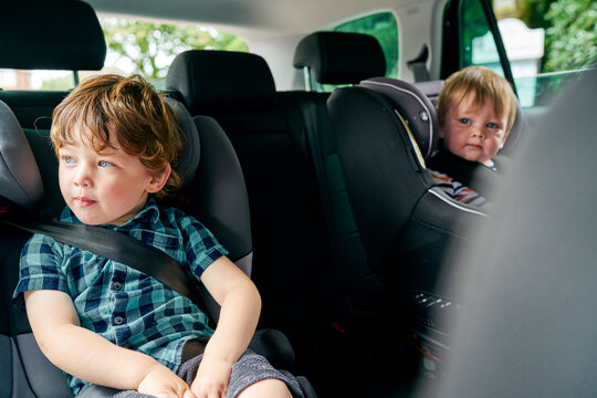 Brothers strapped onto child car seats in the back seat of a family car. 