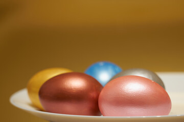 Painted eggs on a white plate with golden background.