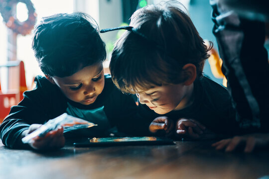 Two children standing next to a table looking at a computer tablet.