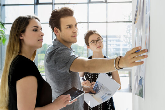Three young architects standing at whiteboard, discussing design ideas.