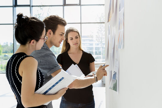 Three young architects standing at whiteboard, discussing design ideas.
