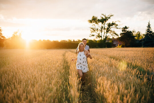 Smiling young couple walking through golden wheat field at sunset. 