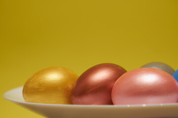 Painted eggs on a white plate with a yellow background.