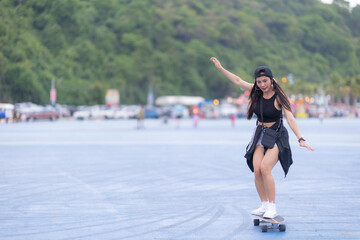 Asian woman playing surf skate or skates board outdoors on beautiful summer day. Happy young women play surf skate at park on morning time in the park.