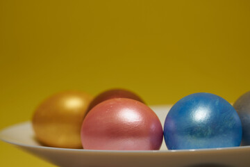 Painted eggs on a white plate with a yellow background.