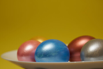 Painted eggs on a white plate with a yellow background.