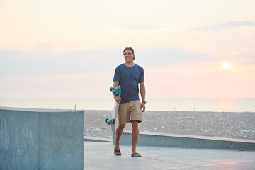 Young man with his skateboard by the beach at sunset. 