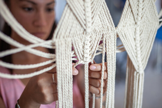 Close up of woman working on cream coloured macrame curtain. 