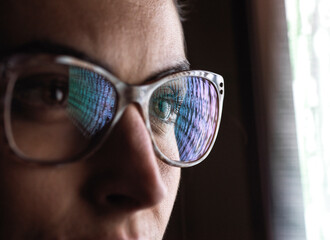 Female data analyst looking at data on screen, reflection in glasses.