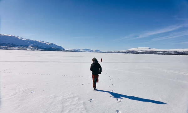 Rear view of two boys running across frozen lake in Vasterbottens Lan, Sweden.