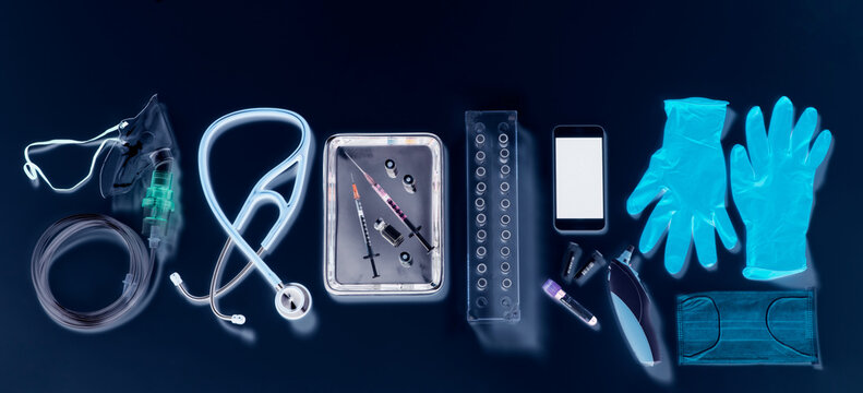 Potential way out of lockdown stage. Medical equipment on a black background, oxygen mask, stethoscope, mobile phone with a contact tracing app, syringes for vaccine, blue gloves and digital thermometer.