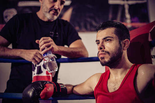 Portrait of boxing coach and male boxer sitting in boxing ring.