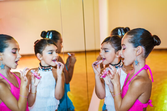 Young girls in dance class, getting ready for a performance, standing in front of mirror, applying lipstick.