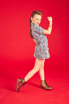 Portrait Of Brunette Girl Wearing Blue Dress And Combat Boots On Red Background.