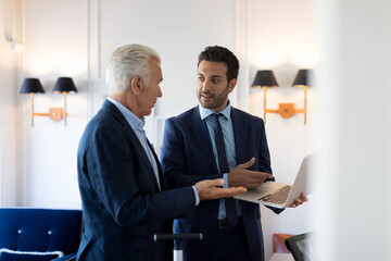 Two businessmen standing indoors, talking.