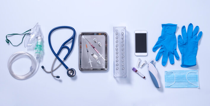 Potential way out of lockdown stage. Medical equipment on a grey background, oxygen mask, stethoscope, mobile phone with a contact tracing app, syringes for vaccine, blue gloves and digital thermometer.