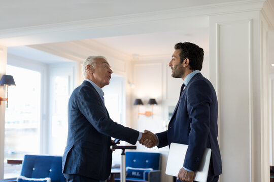 Two businessmen standing indoors, shaking hands.